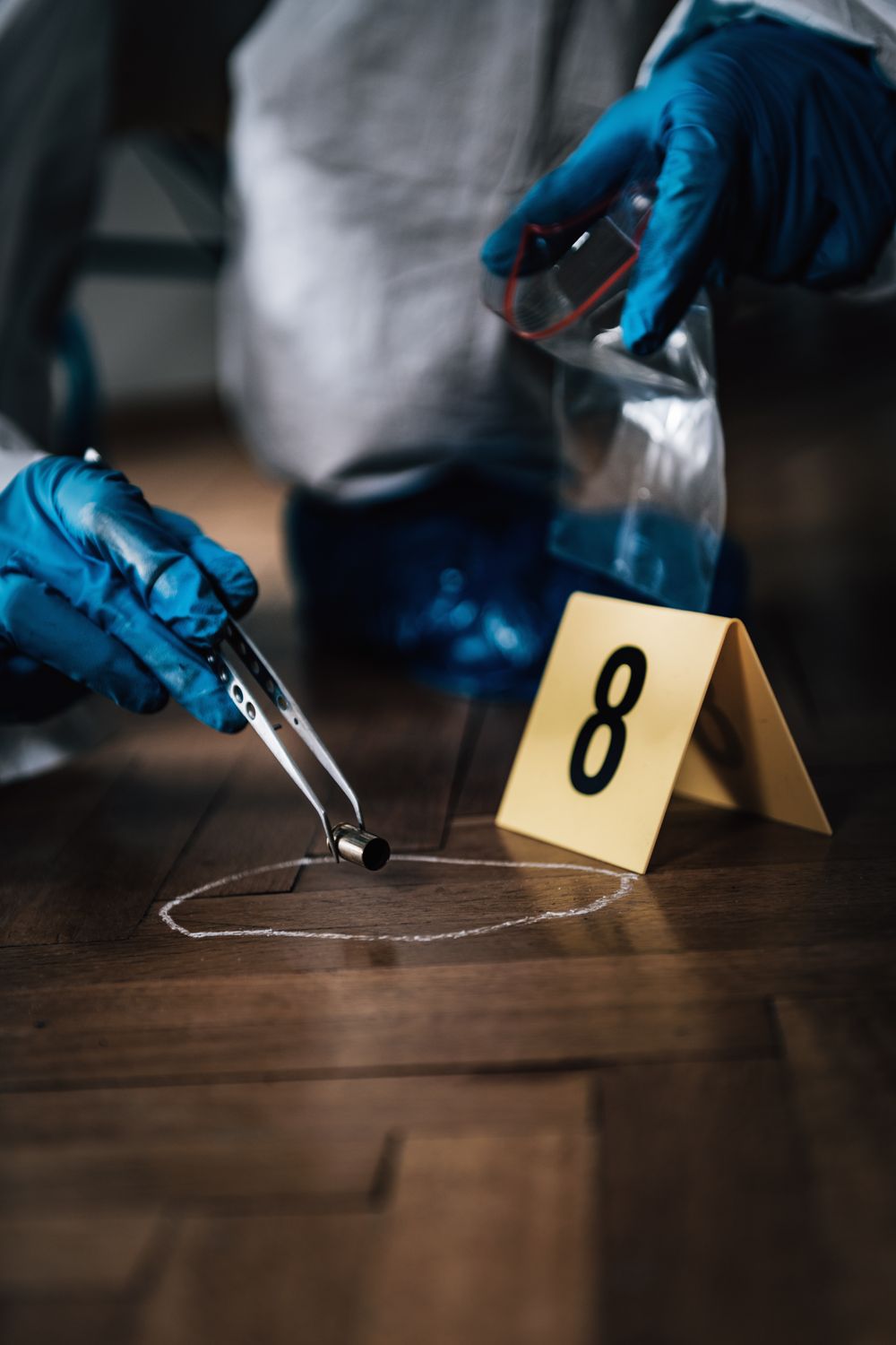 Handen met handschoenen verzamelen bewijs met een pincet naast een genummerde markering